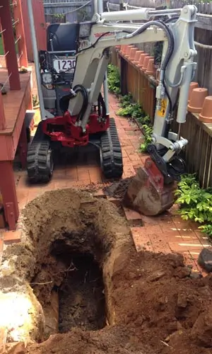 A narrow-access excavator digging a trench for small excavations work in a tight residential space, provided by Earthworks Hawkes Bay.
