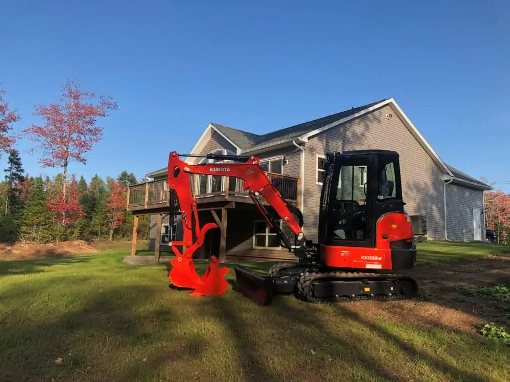 A red Kubota mini excavator parked on a residential lawn, ready for small excavations work by Earthworks Hawkes Bay.
