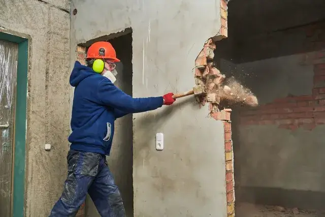 A worker in protective gear demolishing an interior wall with a sledgehammer, showcasing Earthworks Hawkes Bay's expertise in Demolition Work.